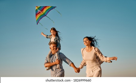 Happy Family Concept. Young Attractive Mother, Handsome Father And Their Little Cute Daughter Having Fun Together On The Beach. Running With A Colorful Kite