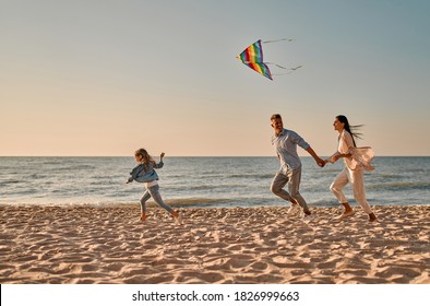 Happy family concept. Young attractive mother, handsome father and their little cute daughter having fun together on the beach. Running with a colorful kite - Powered by Shutterstock