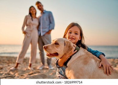 Happy family concept. Young attractive mother, handsome father and their little cute daughter standing together on the beach with dog. - Powered by Shutterstock