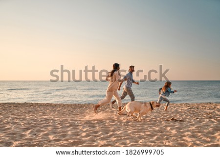 Happy family concept. Young attractive mother, handsome father and their little cute daughter having fun together on the beach and running with dog.