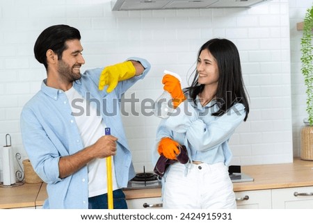 Happy family concept Young happy couple having fun while doing cleaning kitchen, They hold a mops and rags with spray bottle in hands and happily teasing each other.