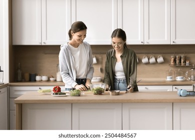 Happy family cooking dinner spend time in kitchen, caring teen daughter helps mother preparing vegetable salad, communicate, enjoy culinary hobby, keep healthy lifestyle, use organic natural products - Powered by Shutterstock