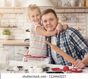 Happy family cooking together in kitchen. Cute girl hugging her dad, smiling at camera