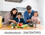 Happy family cooking together on kitchen. Mother Son and daughter with father cooking. Son and mother chopping green vegetables. Home recreation and food preparation on weekend