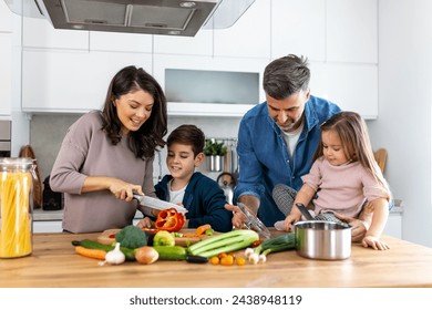 Happy family cooking together on kitchen. Mother Son and daughter with father cooking. Son and mother chopping green vegetables. Home recreation and food preparation on weekend - Powered by Shutterstock