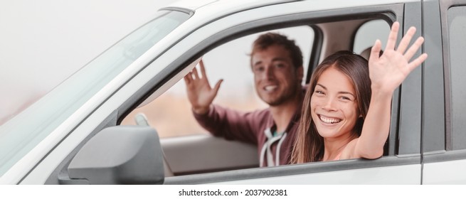 Happy Family Couple Driving. Asian Woman Driver And Passenger Man Waving Hi On Road Trip In New Car. Panoramic Banner People Lifestyle.