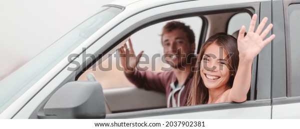 Happy family couple driving. Asian woman\
driver and passenger man waving hi on road trip in new car.\
Panoramic banner people\
lifestyle.