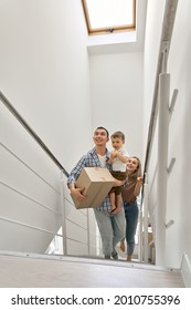 Happy Family Couple New Home Owners With Toddler Kid Child Son Carrying Cardboard Boxes Going Up Stairs On Moving Day Arriving Into New Home. Relocation, Real Estate Property Purchase, Removal.