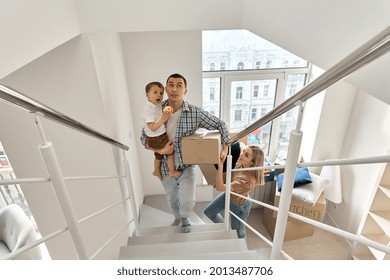 Happy Family Couple New Home Owners With Toddler Kid Child Son Carrying Cardboard Boxes Going Up Stairs On Moving Day Arriving Into New Apartment. Relocation, Mortgage, Property Purchase, Removal.