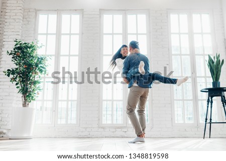 Happy family couple playing fool, dancing and spinning together in bright and spacious loft