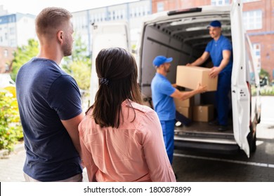 Happy Family Couple Watching Movers Unload Boxes From Truck