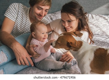 Happy Family With Cute Baby Playing With Jack Russel Dog In Bed At Home.