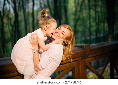Happy family. Cute daughter kisses her mother while sitting at the bridge banister