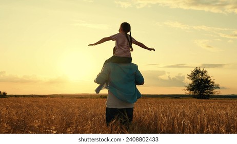 Happy family dad kid playing pilot in field. Kid on dad shoulders, holding hands, in field with ripe wheat. Dad run through field with ears wheat, holding daughter on shoulders. Concept kids dream fly - Powered by Shutterstock