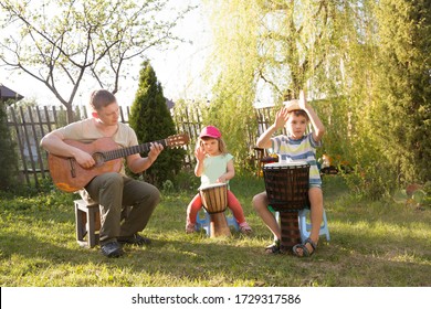 Happy Family Dad And Two Kids Having Fun With Musical Instruments Together Outdoors. Dad Playing  Guitar And Kids Playing Ethnic Drums. Quarantine. Musical Concept