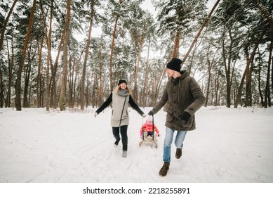 Happy Family With Daughter Having Fun In Winter Forest. Mom, Dad, Daughter Running And Walking In The Snow In Mountains. Father, Mother, And Child In Sled Walk And Play In The Park. Winter Holidays.