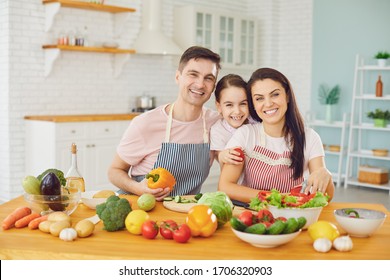 Happy Family With Daughter In The Kitchen With Vegetables Look At The Camera.