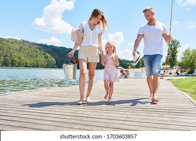 Happy Family With Daughter While Walking On A Footbridge At The Lake In Summer