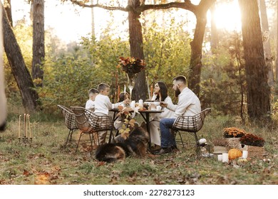 Happy family day. Young dad, mom, child daughter, two little sons, big dog have picnic and sitting by the table in autumn park. Children day. Concept of family coziness, relationships, communication. - Powered by Shutterstock