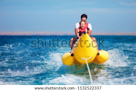 happy family, delighted father and son having fun, riding on banana boat during summer vacation