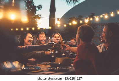 Happy Family Dining And Tasting Red Wine Glasses In Barbecue Dinner Party - People With Different Ages And Ethnicity Having Fun Together - Youth And Elderly Parents And Food Weekend Activities Concept