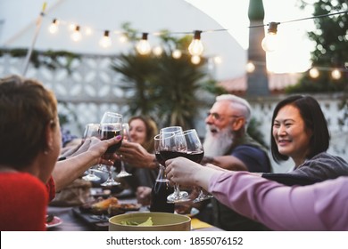 Happy Family Dining And Tasting Red Wine Glasses In Barbecue Dinner Party - People With Different Ages And Ethnicity Having Fun Together - Soft Focus On Glass