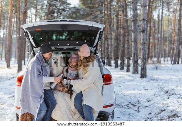 Happy
family with dog on vacation during the winter holidays near road.
Dressed in warm clothes sitting on the trunk of a car and drinking
tea from a thermos. space for text. Winter
vacation