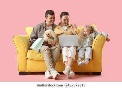 Happy family with dog shopping online on sofa against pink background - Powered by Shutterstock