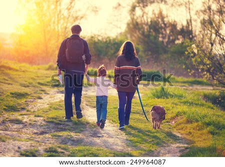 Happy family with dog walking in the village at sunset  back to camera