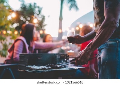 Happy Family Doing Barbecue Dinner On Rooftop At Night - Close Up Hand Of Tattoo Man Cooking At Bbq Grill Outdoor - Concept Of Food, People Lifestyle And  Summer Weekend Activities 