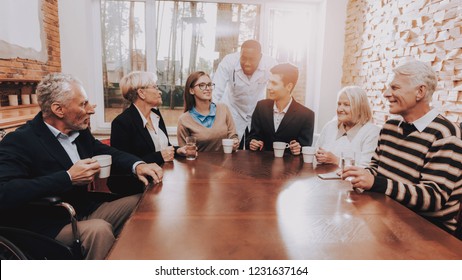 Happy Family Drink Different Drinks. Doctor At Head Of Table. Young And Old People Sit Together. Room In Nursing Home. Children Visit Grandparents. Patients Talk With Each Other. Parents In Good Mood.