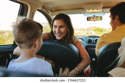 Happy Family Driving In A Car. Woman Playing With Her Children Sitting In Backseat Od The Car.