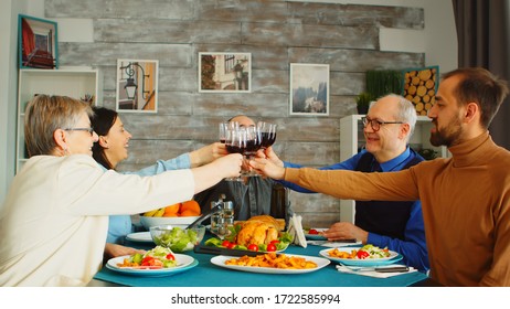 Happy Family During Lunch Toasting With Red Wine. Friends And Family At Sunday Dinner