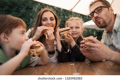 happy family eating burgers sitting at a table in a cafe