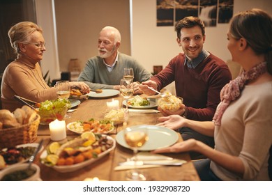 Happy Family Eating Dinner At Dining Table. Focus Is On Young Man Serving Food To His Wife. 