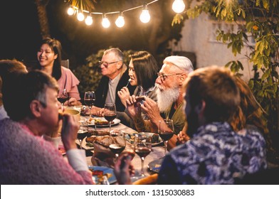 Happy Family Eating And Drinking Wine At Barbecue Dinner Outdoor - Multiracial Mature And Young People Having Fun At Bbq Sunday Meal - Food And Summer Lifestyle Concept - Focus On Tattoo Man Hands