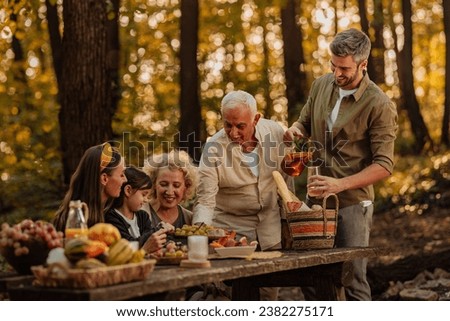 Happy family is eating fruits, croissants and drinking ice tea while having a picnic in the woods