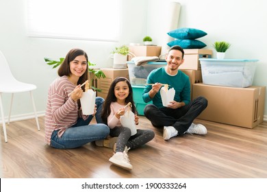 Happy Family Eating Take Out Food While Sitting On The Floor. Attractive Young Wife, Husband And Daughter Taking A Break From Unpacking In Their New Home