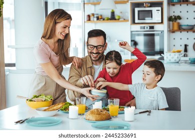 Happy family eating together in the kitchen. Dad and boy take tomatoes. Everyone is happy and satisfied. Home recreation and food preparation on weekends. The concept of community and enjoyment - Powered by Shutterstock