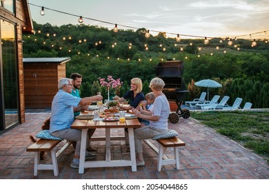 Fröhliche Familie, die zusammen draußen isst. Lächelnde Generation Familie sitzt am Esstisch während des Abendessens. Herzlichen Glückwunsch an die Familie, die gemeinsam im Garten speist.