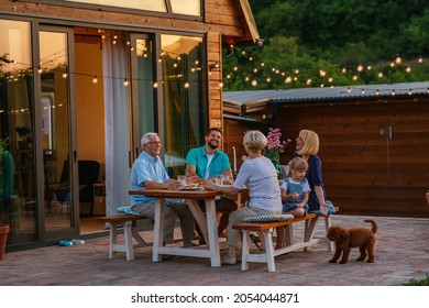 Fröhliche Familie, die zusammen draußen isst. Lächelnde Generation Familie sitzt am Esstisch während des Abendessens. Herzlichen Glückwunsch an die Familie, die gemeinsam im Garten speist.