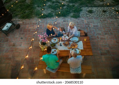 Happy Family Eating Together Outdoors. Smiling Generation Family Sitting At Dining Table During Dinner. Happy Cheerful Family Enjoying Meal Together In Garden. View From Above