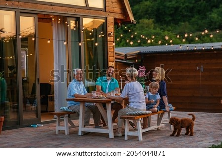 Happy family eating together outdoors. Smiling generation family sitting at dining table during dinner. Happy cheerful family enjoying meal together in garden.