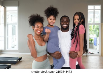 Happy Family Enjoy Holiday Together In Fitness Center. Young Father Hold Both Of His Daughter In Arms While The Mother Raise Her Fist Up.