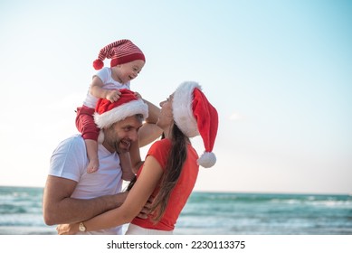 happy family enjoy on beach in vacation, holiday in new year and Christmas. son on shoulder of father, fun and happiness near sea together. white and red clothes and Santa hats. - Powered by Shutterstock