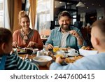 Happy family enjoying conversation at dining table during a breakfast while staying at the hotel. Focus is on parents. 