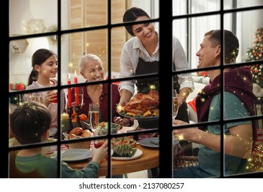 Happy Family Enjoying Festive Dinner At Home, View Through Window. Christmas Celebration