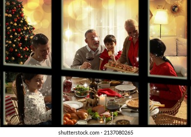 Happy Family Enjoying Festive Dinner At Home, View Through Window. Christmas Celebration