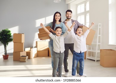 Happy family enjoying relocating to new apartment concept. Young smiling family with small children son and daughter standing together in new flat feeling cheerful with raised hands during relocating