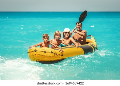 Happy Family Is Enjoying A Ride In Rubber Kayak And Waves Are Splashing Them At Tropical Ocean Water During Summer Vacation.